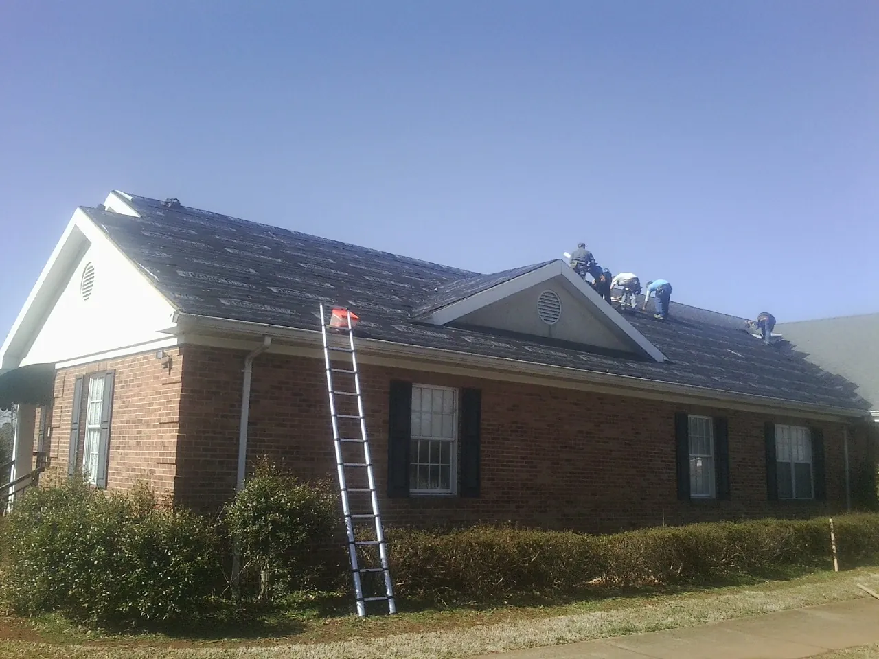 Crew tearing shingles off a brick ranch roof with a ladder set — Metal Roof Repair work by our crew in Beach City
