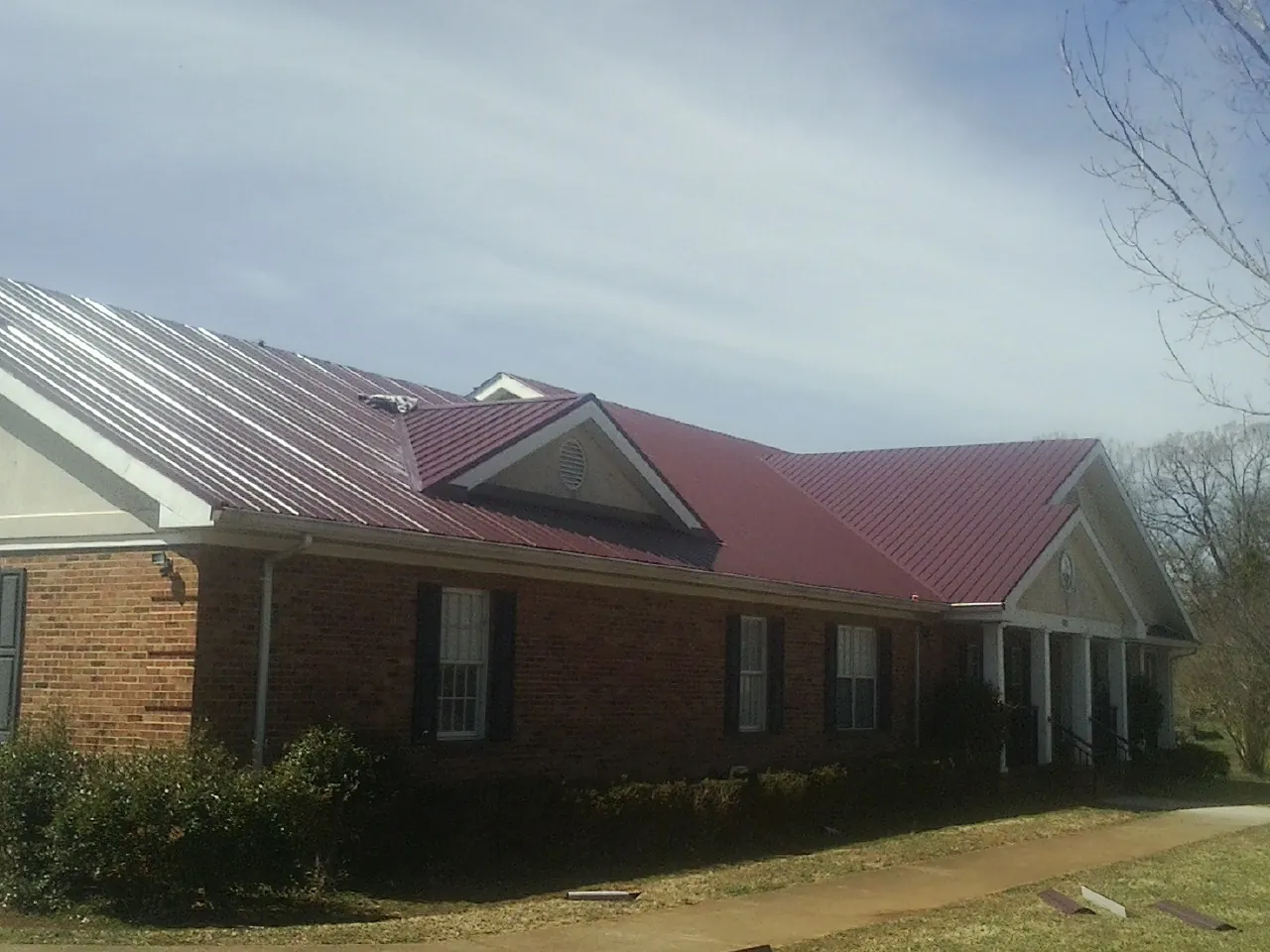 Red metal roof with gabled entries on a long brick building, from a Hail Damage Roof Repair job in Beach City