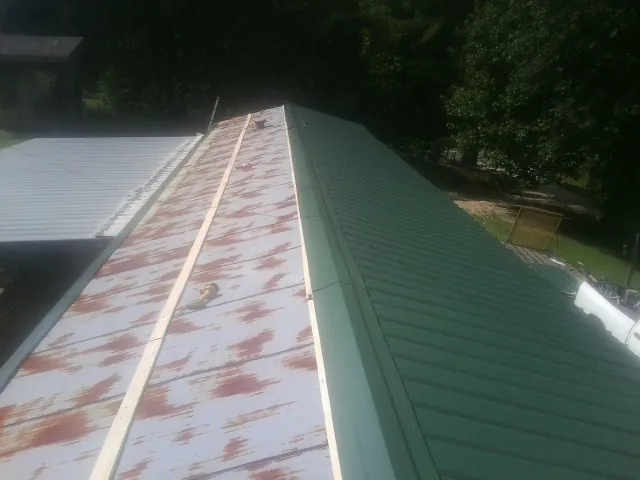 Old rusted panels beside newly installed green metal roofing — Wind Damage Roof Repair by Roofing Brothers in Beach City