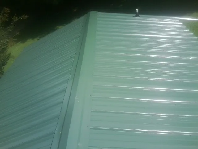 New green metal panels meeting at the ridge of a roof — Flat Roof Repair work by our crew in Beach City