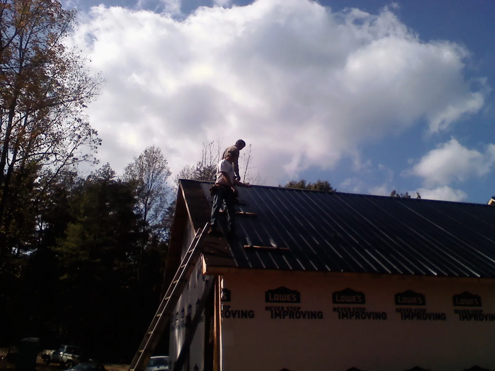 Roofer fastening dark metal panels high against a cloudy sky, from a Roof Inspection job in Beach City