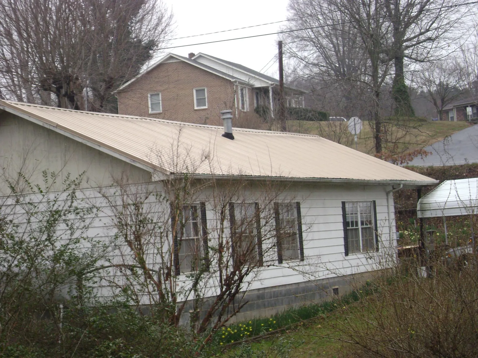 Tan metal roof on a white sided house set into a hillside — Commercial Roofing by Roofing Brothers in Beach City