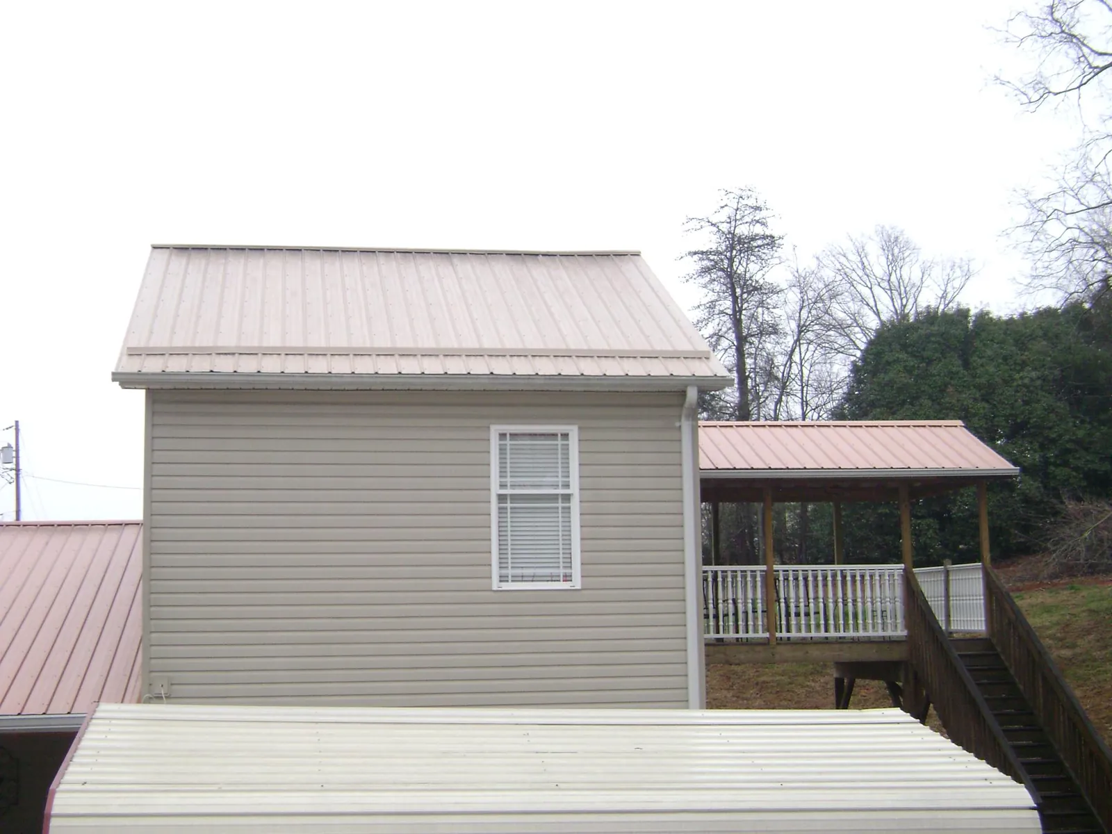 Tan metal roofs on a two story addition and attached porch, from a Roof Replacement job in Beach City